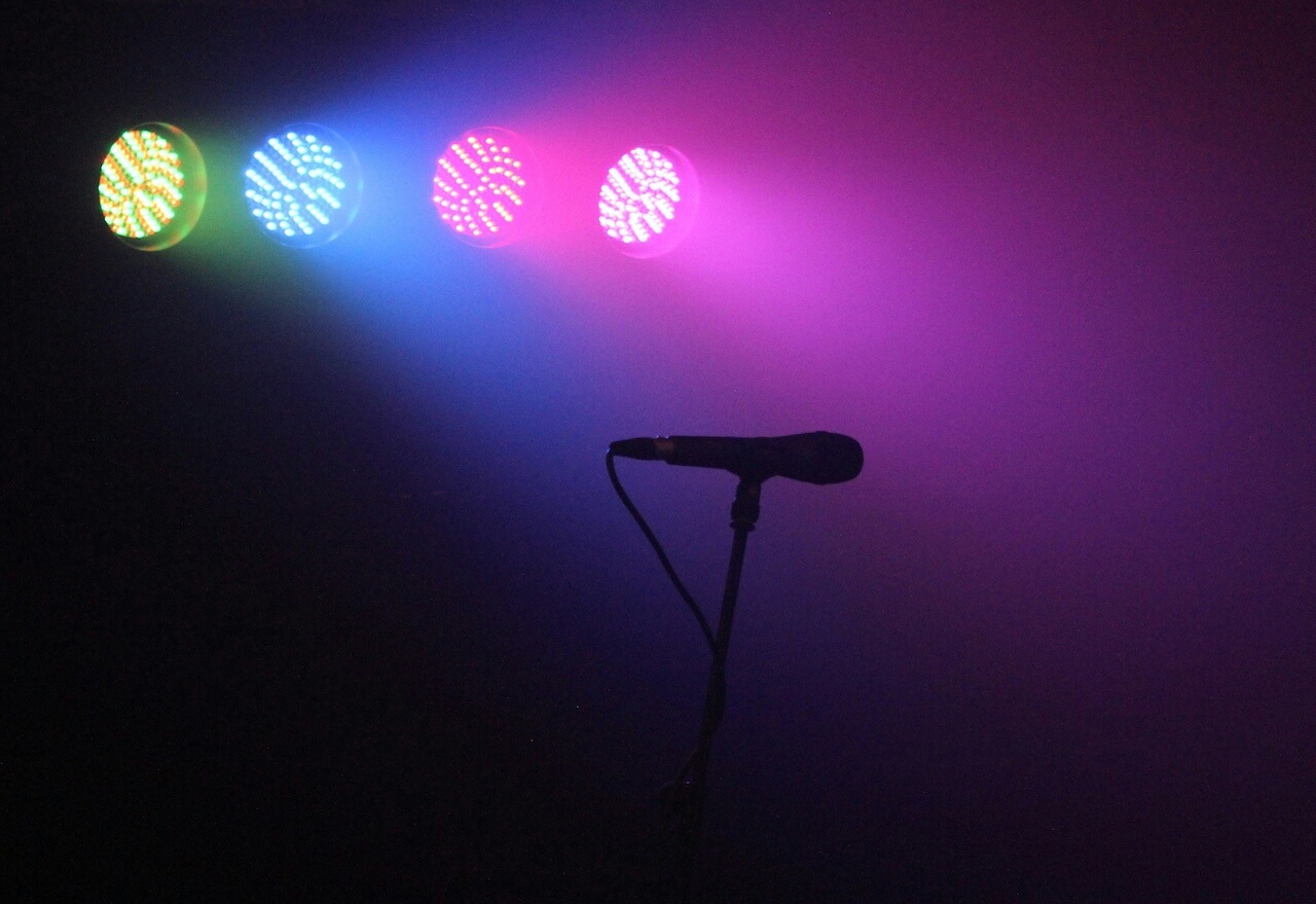 A picture of a microphone in a dark room, illuminated by a few colorful lights.